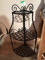 Full view of matte black 3-tier corner plant stand showing scrollwork and lattice shelves