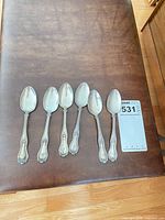 Six sterling silver teaspoons lined on brown surface
