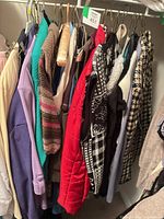 Group of hanging garments showing cardigans, red quilted vest and other pieces