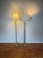 Pair of metal floor lamps standing side by side, cords visible