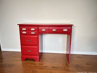 Front view of red writing desk showing all drawers and hardware