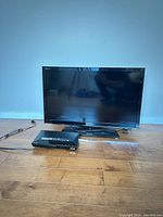 Front view of Sony 32" LCD TV on stand with Blu-ray player and cords on floor
