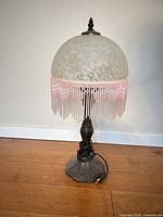 Front view of complete lamp showing glass shade, pink beaded fringe, metal base, attached cord