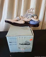 Full view of figurine on pillow with wings, resting on original box