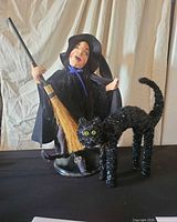 Witch doll with broom on stand beside black tinsel cat