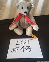 Full view of grey Steiff bear with red ribbon, ear tag visible