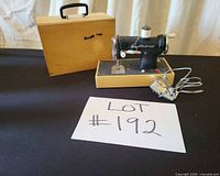Toy sewing machine on wood base, wooden case, foot pedal and cord visible
