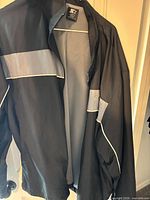 Front view of black outer shell jacket, grey stripe, mesh lining and brand tag visible