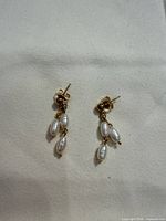 Pair of gold-tone stud earrings with three rice pearls each displayed on fabric background