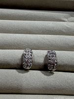 pair of silver-tone pavé crystal huggie earrings on display pad, showing front stone detail