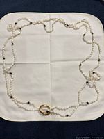 Full view of continuous pearl necklace arranged on cloth showing gold-tone ring and black accent beads