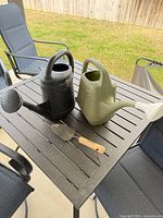 Lot overview on patio table: both watering cans and hand trowel