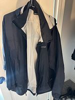 Marmot black shell jacket with light grey interior lining shown hanging open