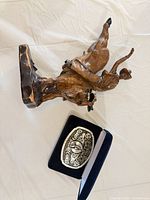 Sculpture lying on side next to buckle in box