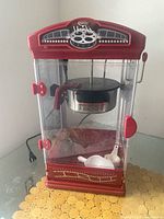 Front view of red popcorn maker with kettle and accessories visible