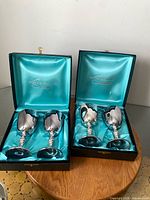 Two open presentation boxes each containing two silver-plated goblets