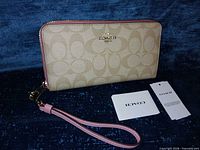 Front view of Coach signature canvas zip-around wallet with pink wrist strap and original tags