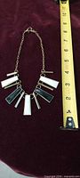Gold-tone necklace with black, white and rhinestone rectangular drops next to tape measure