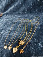 All five gold-tone heart pendant necklaces laid out on blue background