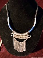 Front view of necklace on display bust showing cord colors, metal coil, and chain fringe