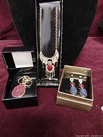 Necklace, keychain, drop earrings and stud earrings presented in boxes