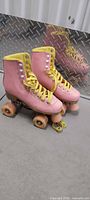side view of both skates showing pink boots, yellow laces, wheels