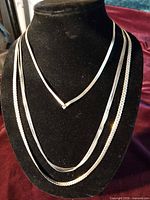 Three gold-tone chain necklaces displayed on black bust