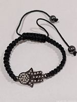 Full view of bracelet showing macrame band, Hamsa charm, and adjustable cords