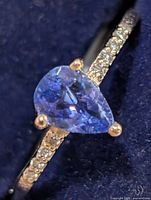 Close-up of ring displaying pear tanzanite and moissanite accents on gold band