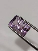 Front view of rectangular faceted amethyst held by tweezers