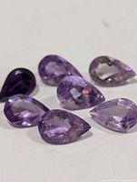 Seven pear-cut purple gemstones on white background