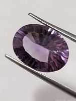 Front view of oval faceted amethyst held by tweezers