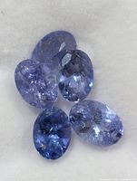 Five oval violet-blue tanzanite gemstones on white background
