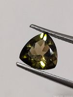 Trillion cut green tourmaline held by tweezers showing facets