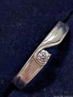 Close-up of silver ring showing wave tension setting and clear stone