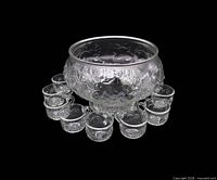 Clear pressed glass punch bowl with twelve matching cups arranged around it