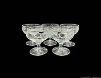 Group of five clear floral etched champagne coupe glasses on black background