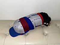 Stack of about 11 blank baseball caps in various colours, tag visible