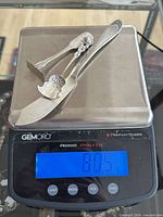 Three sterling silver utensils on digital scale reading 80.5 g