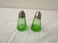 Two green uranium glass shakers with metal tops on tabletop
