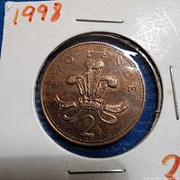 Reverse of 2p coin displaying Prince of Wales feathers and "TWO PENCE" legend, date hidden by holder writing