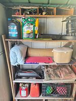 Overall view of shelving with Weed B Gon jug, gas can, lawn edger, crate, rolled mat and other items