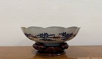 Side view of scalloped porcelain bowl on wooden stand showing exterior blue scrolling pattern