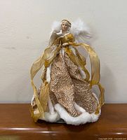Front view of porcelain angel tree topper showing gold gown, ribbons and feather wings