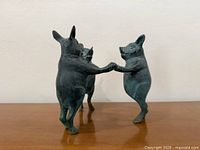 Front view of bronze sculpture showing two pigs facing viewer holding hooves