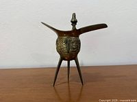 Side view showing full vessel, tripod legs and relief decoration