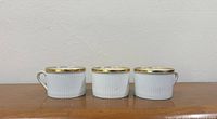 Front view of three ribbed white porcelain tea cups with gold rim and handles