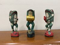 Front view of three carved frog musician figurines