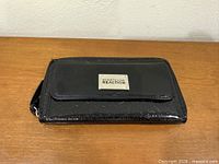 Front view of clutch showing flap pocket, logo plate, wrist strap