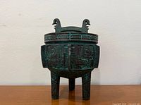 Frontal view of verdigris tripod ice bucket with lid and bird head handles